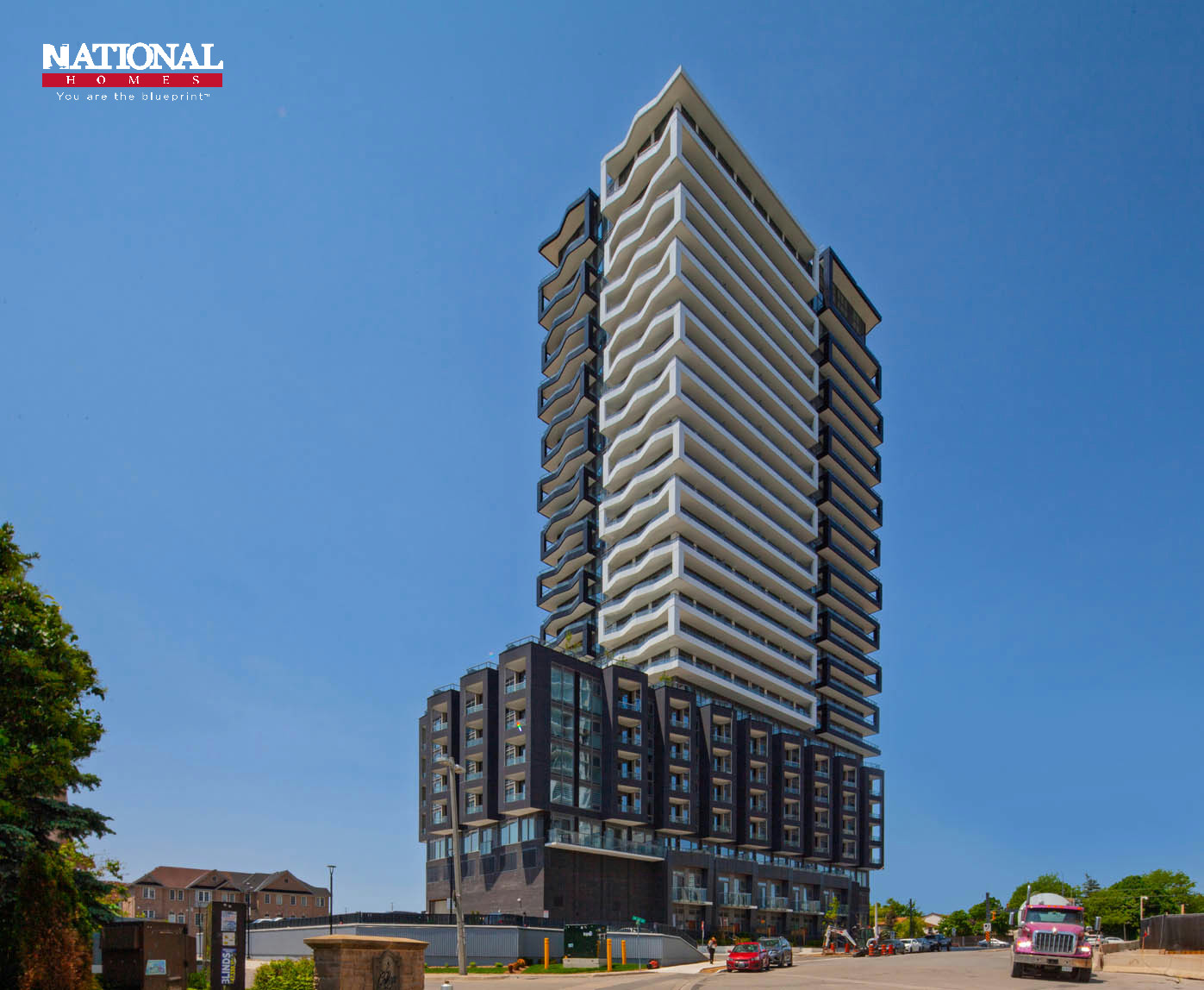 Full-height view of the completed DUO tower and its podium from across the street under a clear blue sky