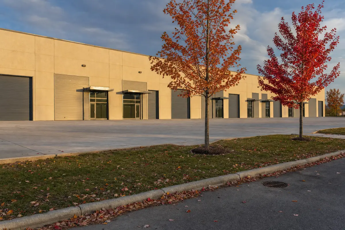 Single-storey multi-tenant industrial building with a row of loading doors and autumn maples